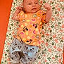 baby, infant, child, lying_down, blanket, floral_pattern, clothing, shirt, pants, socks, mickey_mouse, disney, cute, portrait, indoor, soft_lighting, expression, hand, footwear, fabric