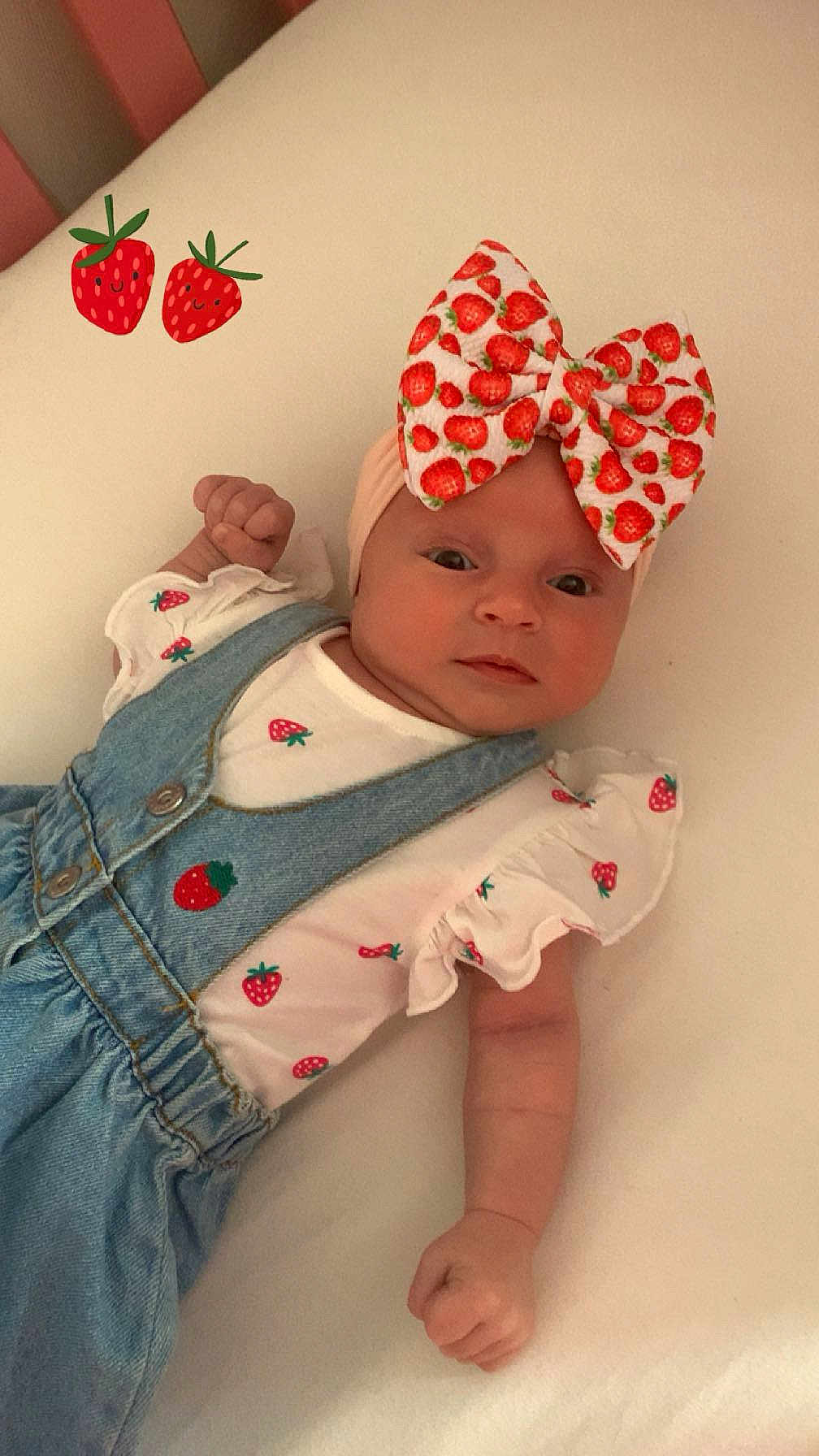 Kalyssa participe au concours pour gagner de l'argent avec cette photo : baby, infant, face, headband, bow, strawberry, clothing, denim, onesie, cute, lying_down, hand, fist, soft_surface, bed, playful, sticker, child, adorable, portrait