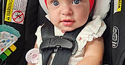 Maelynn joined the competition — help win amazing prizes! baby, car_seat, red_headband, straps, cute, child, infant, sitting, safety, wide_eyes, hand, foot, clothing, white_outfit, indoor, portrait, closeup, seatbelt, warning_label, curious