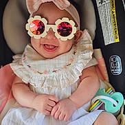 Maelynn is registered to the contest to win money with this photo: baby, infant, sunglasses, headband, bow, car_seat, toy, smile, happy, cute, child, clothing, dress, hand, face, reflection, pink, white, accessory, portrait