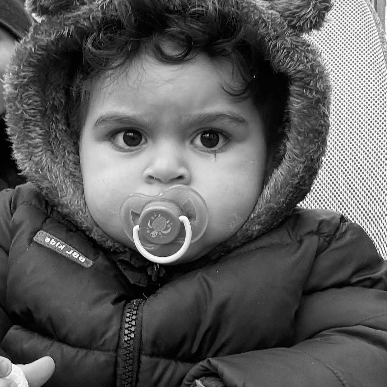 Lorenzo a rejoint le concours — aidez-le/la à gagner de superbes lots ! baby, big_eyes, black_and_white, candid, child, close_up, fur_hood, hand, hood, mesh_seat, outdoor, pacifier, portrait, puffer_jacket, serious_expression, stroller, texture, toddler, winter_coat, zipper