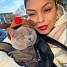Puka is registered to the contest to win money with this photo: blue_sky, building, cat, cute, daylight, face, festive, golden_eyes, hand, holiday, jacket, outdoor, pet_carrier, reindeer_hat, scarf, selfie, smile, tree, winter_clothing, woman