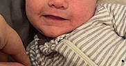 Jameson is registered to the contest to win money with this photo: baby, infant, smile, face, striped_clothing, onesie, hand, blue_eyes, lying_down, soft_surface, cute, young_child, person, portrait, happy, closeup, cozy, indoor, skin, expression