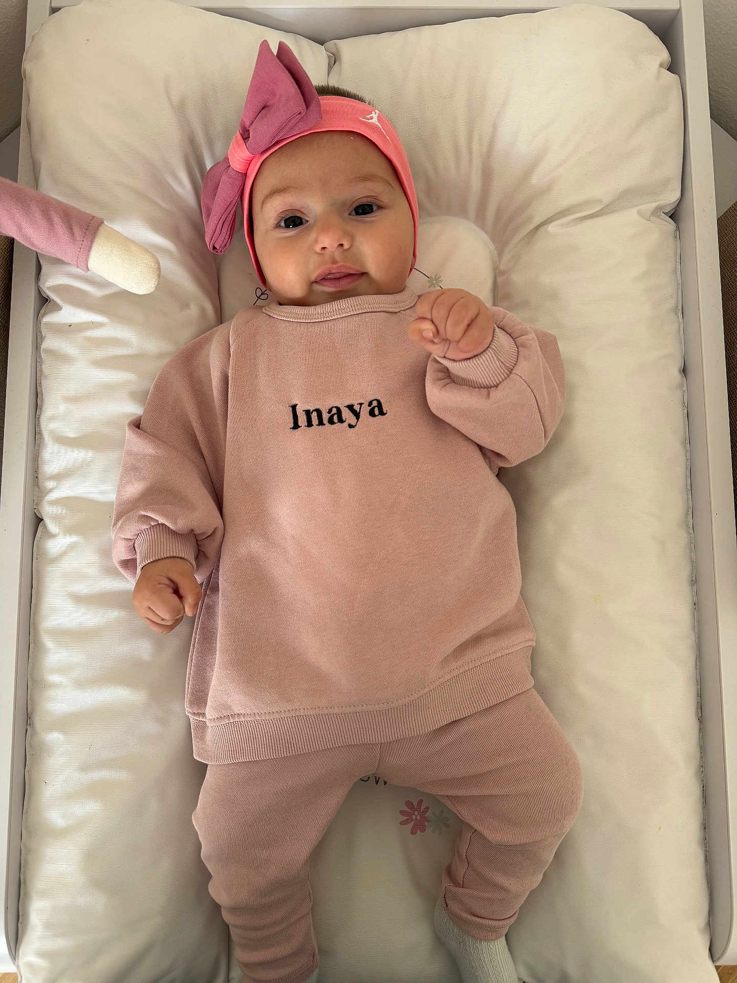 Inaya a rejoint le concours — aidez-le/la à gagner de superbes lots ! baby, infant, pink_clothing, headband, bow, cushion, changing_pad, plush_toy, soft_toy, lying_down, indoors, child, person, smiling, cute, cozy, sleepwear, sock, face, hand