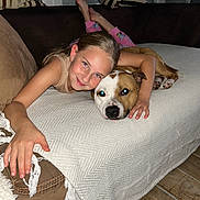 Urkan a rejoint le concours — aidez-le/la à gagner de superbes lots ! girl, dog, couch, blanket, smile, living_room, affection, pets, child, comfort, striped_cushions, flooring, indoor, relaxation, friendship, casual_clothing, resting, human_animal_bond, happy, portrait