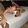 girl, dog, couch, blanket, smile, living_room, affection, pets, child, comfort, striped_cushions, flooring, indoor, relaxation, friendship, casual_clothing, resting, human_animal_bond, happy, portrait