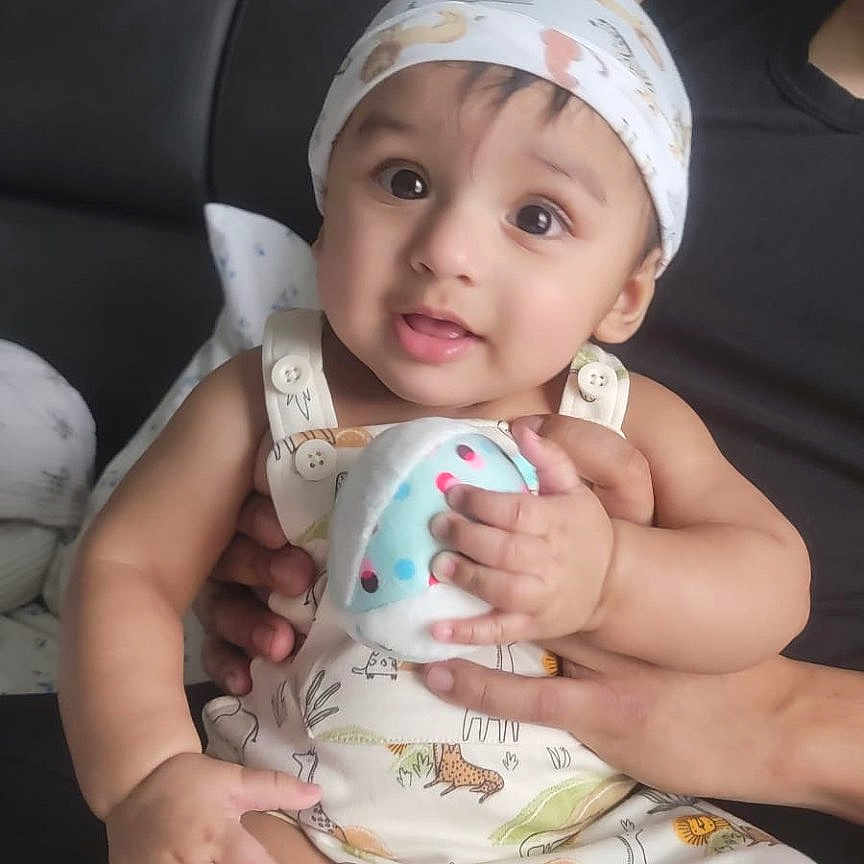 Charvik joined the competition — help win amazing prizes! adult_hand, baby, child, clothing, couch, cute, expression, face, happy, headscarf, indoors, infant, person, plush_toy, portrait, romper, sitting, skin, smiling, toy