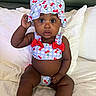 baby, child, infant, hat, swimsuit, cherry_pattern, bed, pillow, white_bedding, cute, portrait, sitting, indoors, skin, expression, hand, summer_clothing, clothing, headwear, person