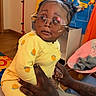 Brooklyn joined the competition — help win amazing prizes! baby, child, glasses, yellow_onesie, hands, playroom, basketball_hoop, calendar, colorful, indoor, person, toy, furniture, adult_hands, expression, cute, baby_clothing, seat, floor, decor