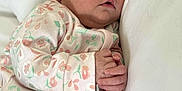 Mariana is registered to the contest to win money with this photo: baby, sleeping, infant, onesie, floral_pattern, pillow, cozy, peaceful, cute, child, soft_lighting, indoors, newborn, resting, hands, face, head, skin, person, portrait