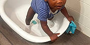 James is registered to the contest to win money with this photo: baby, baby_clothing, blue_cloth, child, curious, floor, grip, holding, indoor, looking_up, onesie, person, plastic_tub, socks, standing, striped_clothing, tiled_wall, toddler, wood_floor, young_child