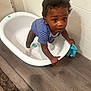 James is registered to the contest to win money with this photo: toddler, child, baby, onesie, striped_clothing, plastic_tub, floor, wood_floor, tiled_wall, socks, blue_cloth, indoor, standing, holding, curious, person, young_child, baby_clothing, grip, looking_up