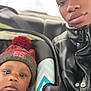 James is registered to the contest to win money with this photo: baby, child, car_seat, winter_hat, pom_pom, adult, leather_jacket, car_interior, portrait, closeup, seatbelt, person, face, window, winter_clothing, indoor, transport, casual, family, travel
