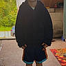 child, boy, smiling, portrait, standing, outdoor, porch, doorway, house, hoodie, shorts, shoes, clogs, clothing, face, person, yard, trees, rug, daylight