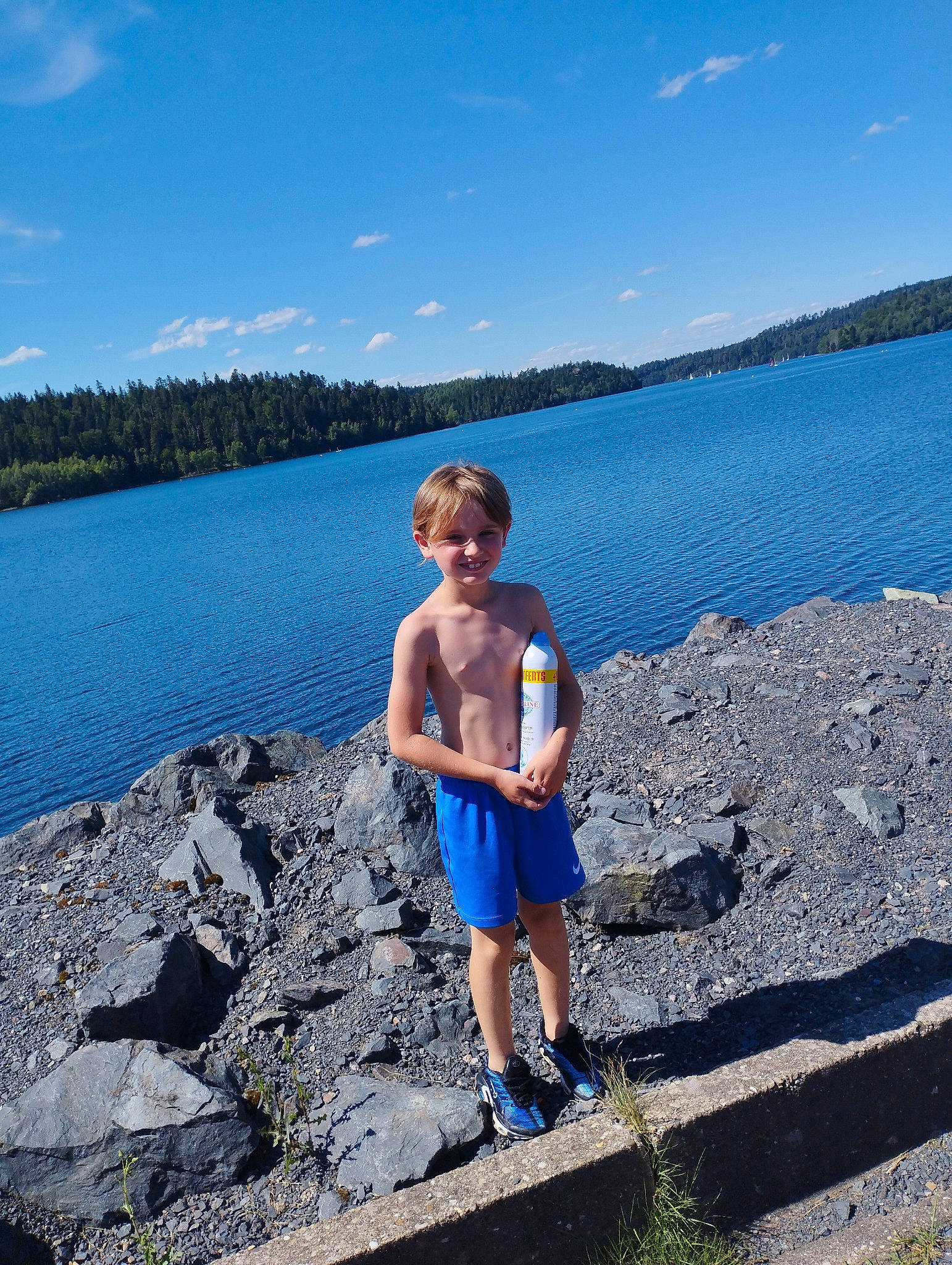 Liam a rejoint le concours — aidez-le/la à gagner de superbes lots ! azure, bank, blue, cloud, coastal_and_oceanic_landforms, fun, highland, horizon, joy, lake, leisure, mountainous_landforms, natural_environment, people_in_nature, person, shorts, sky, summer, tree, water