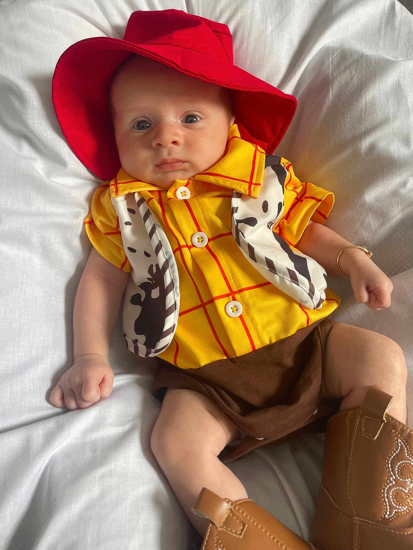 Bobby Lee is registered to the contest to win money with this photo: baby, child, cowboy_costume, red_hat, yellow_shirt, cow_print_vest, brown_shorts, cowboy_boots, infant, portrait, cute, costume, hat, footwear, lying_down, white_blanket, person, indoors, fashion, accessory