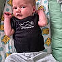 baby, infant, onesie, black_clothing, mustache_graphic, text_on_clothing, teddy_bear_pattern, blanket, lying_down, curious_expression, arms_up, face, head, person, soft_fabric, bed, pajamas, cute, indoor, child