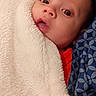 baby, infant, child, portrait, face, eyes, wide_eyed, lying_down, blanket, fluffy_blanket, bedding, red_clothing, blue_fabric, patterned_fabric, indoor, close_up, cozy, awake, photograph, home