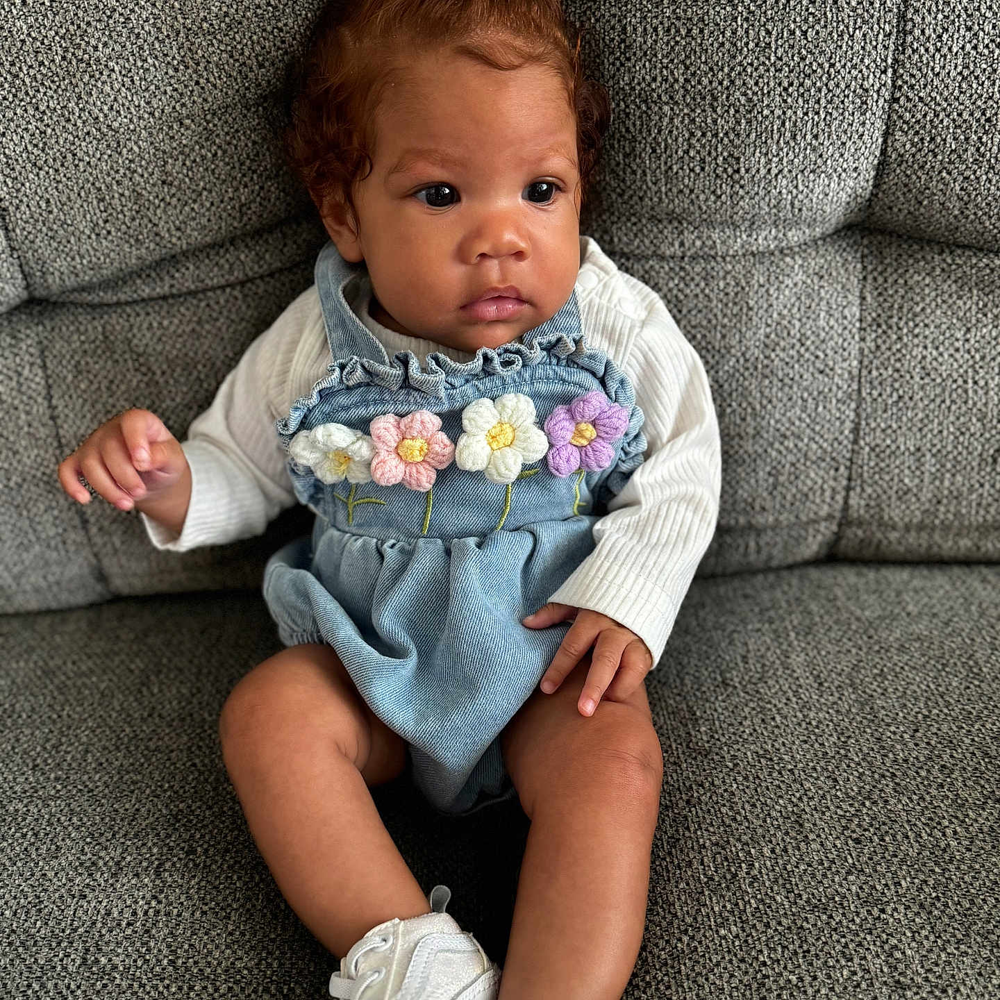 Olivia is registered to the contest to win money with this photo: baby, bow, casual, child, clothing, crocheted_flowers, curly_hair, cute, denim_romper, footwear, gray_couch, indoor, infant, looking_away, portrait, sitting, small_hands, textured_fabric, thoughtful, white_sneakers