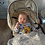 Rudi is registered to the contest to win money with this photo: baby, stroller, toy, blanket, indoor, child, face, clothing, floor, cabinet, wooden_floor, person, infant, warm, comfort, cute, portrait, sitting, expression, baby_clothes