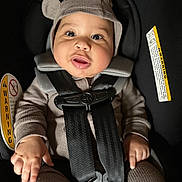 Karmelo is registered to the contest to win money with this photo: baby, car_seat, child, infant, seatbelt, hat, knitwear, warning_label, cute, face, hands, safety, straps, indoors, person, young_child, clothing, headwear, closeup, expression