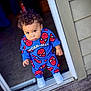 toddler, child, boy, standing, doorway, blue_clothing, spiderman_outfit, curly_hair, white_shoes, wooden_deck, house_siding, indoors, outdoors, portrait, looking_up, casual, cute, young_child, fashion, expression