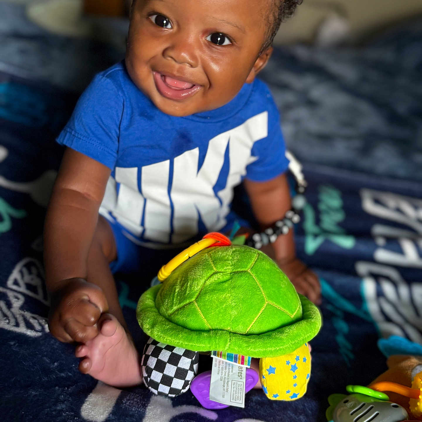 Deason joined the competition — help win amazing prizes! baby, blanket, blue_shirt, bright_colors, child, closeup, cute, happy, indoors, infant, nike, playtime, plush_turtle, rattle, sitting, smiling, soft_toys, toddler, toy, young_child