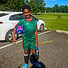 Josh is registered to the contest to win money with this photo: child, soccer_ball, sportswear, water_bottle, car, parking_lot, green_field, trees, blue_sky, sunny_day, soccer_cleats, grass, person, outdoor, smiling, shorts, socks, athlete, recreation, activity