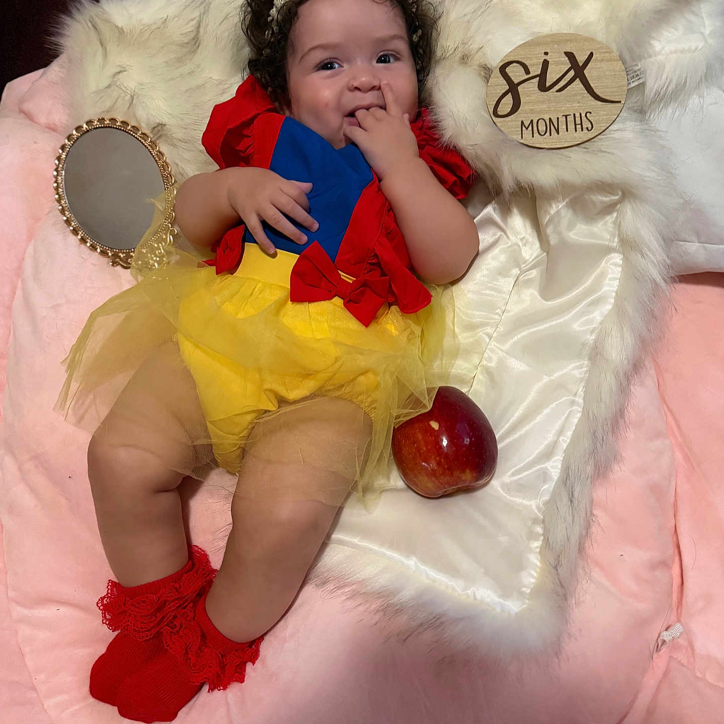 Lisa joined the competition — help win amazing prizes! baby, infant, six_months, snow_white_costume, red_bow, yellow_tutu, red_socks, curly_hair, apple, mirror, fur_blanket, pink_blanket, cute, smiling, playful, portrait, child, soft_lighting, indoor, costume