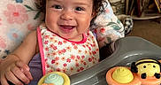 Lisa joined the competition — help win amazing prizes! baby, bee_toy, bib, blanket, child, clothing, curly_hair, cute, face, happy, high_chair, indoor, infant, person, playful, portrait, smiling, sun_toy, table, toy