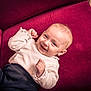 baby, smiling, infant, child, couch, red_couch, clothing, sweater, pants, happy, portrait, indoor, furniture, person, cute, relaxed, cozy, skin, head, hands