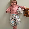 Allison joined the competition — help win amazing prizes! baby, child, smiling, portrait, indoors, lying_down, knit_hat, pink_clothing, pajamas, patterned_clothing, teddy_bear, stuffed_animal, toy, floral_hat, infant, face, hands, feet, wall, ai_generated_content