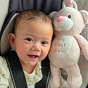 Allison is registered to the contest to win money with this photo: baby, infant, child, smiling, happy, portrait, car_seat, seatbelt, plush_toy, teddy_bear, pink, indoors, close_up, face, eyes, mouth, clothing, sweater, vehicle, photography