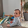 baby, bottle, child, curious, cute, face, floor, furniture, home, indoor, person, plant, play_area, portrait, striped_shirt, table, toddler, toy, window_light, young_child