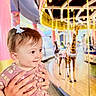 baby, child, hands, carousel, giraffe, amusement_ride, indoor, lights, smile, hair_bow, pink_dress, patterned_clothing, person, portrait, happy, playful, colorful, fun, family, holding
