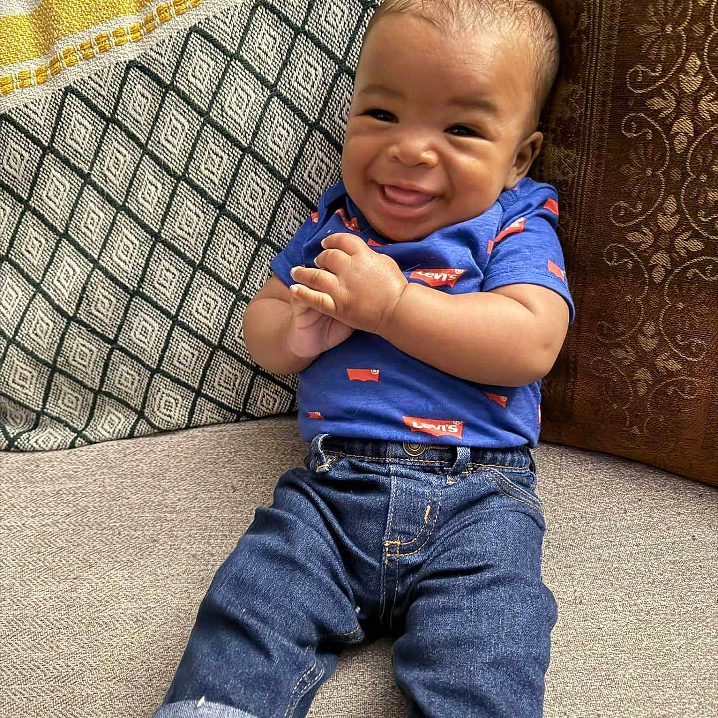 Amirion is registered to the contest to win money with this photo: baby, blue_shirt, casual_clothing, child, couch, cozy, fabric, hands, happy, indoor, infant, jeans, levis, patterned_pillow, pillow, portrait, rolled_jeans, smiling, socks, texture