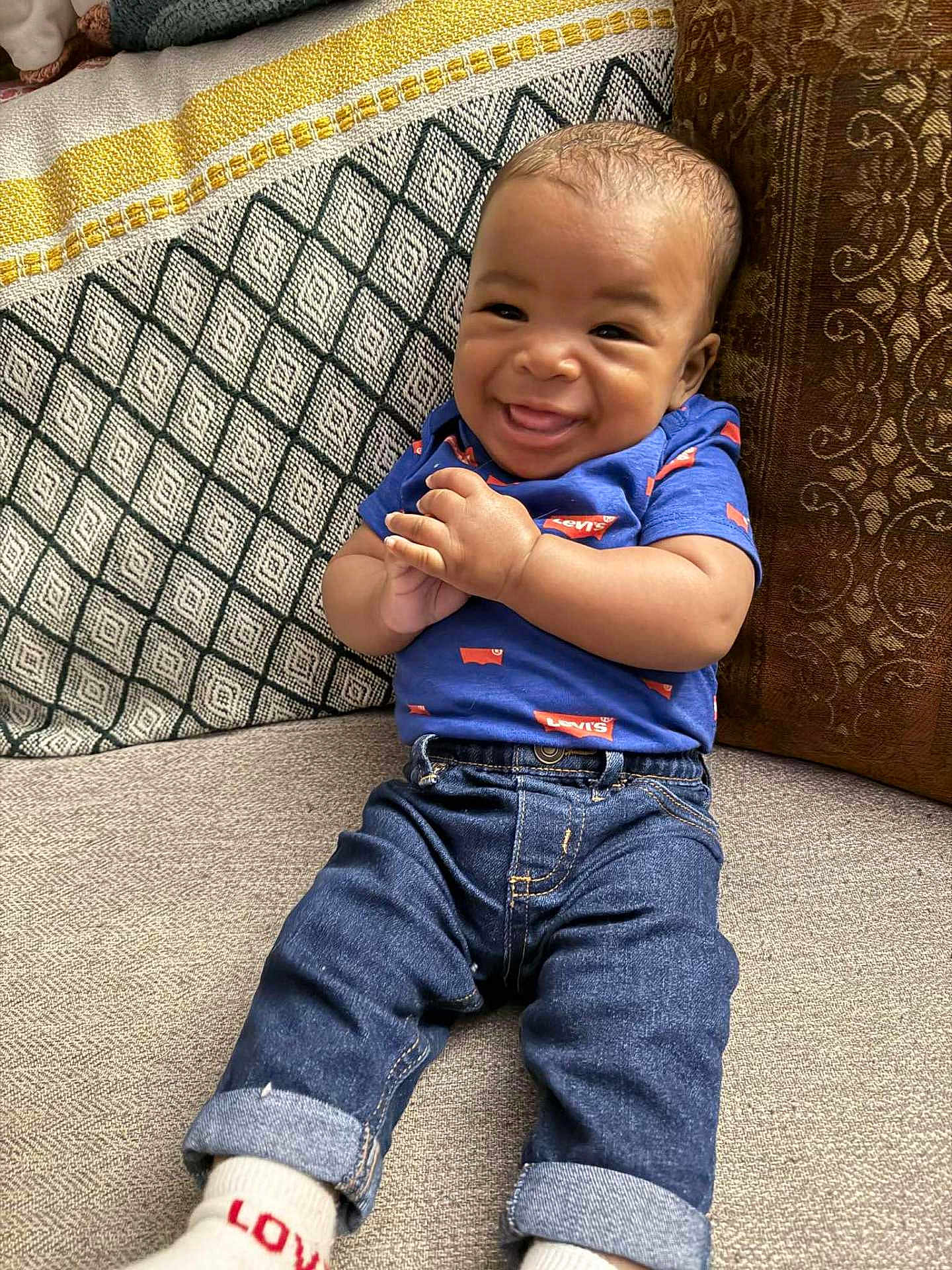 Amirion is registered to the contest to win money with this photo: baby, smiling, jeans, blue_shirt, levis, couch, pillow, cozy, hands, rolled_jeans, socks, happy, infant, child, portrait, indoor, fabric, texture, patterned_pillow, casual_clothing