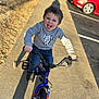 child, boy, bicycle, training_wheels, sidewalk, gray_hoodie, jeans, playful, tongue_out, sunlight, shadow, parking_lot, cars, outdoor, happy, smiling, person, concrete, casual_clothing, daytime