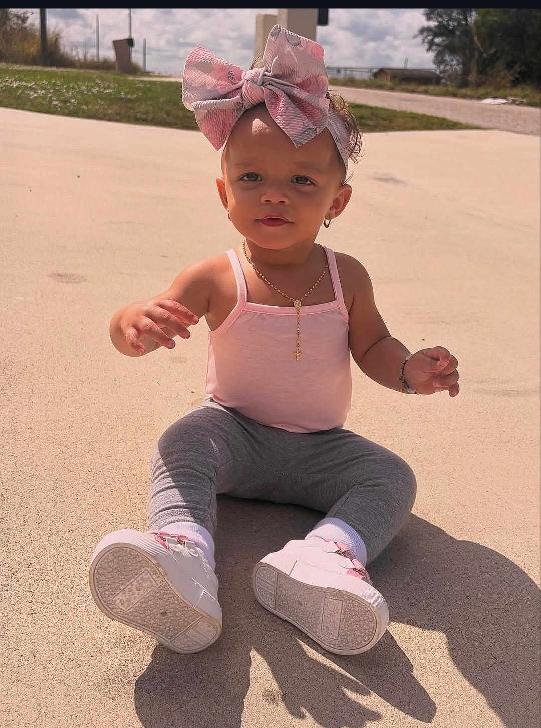 Ilaria is registered to the contest to win money with this photo: child, toddler, pink_bow, tank_top, leggings, white_shoes, outdoor, concrete, sunlight, shadow, necklace, bracelet, earrings, cute, baby, sitting, curious, daytime, casual_clothing, portrait
