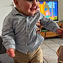 Charly a rejoint le concours — aidez-le/la à gagner de superbes lots ! baby, child, toddler, smile, button_up_shirt, pants, standing, adult_hand, living_room, television, cartoon, wooden_furniture, tile_floor, couch, portrait, cute, happy, indoor, face, person