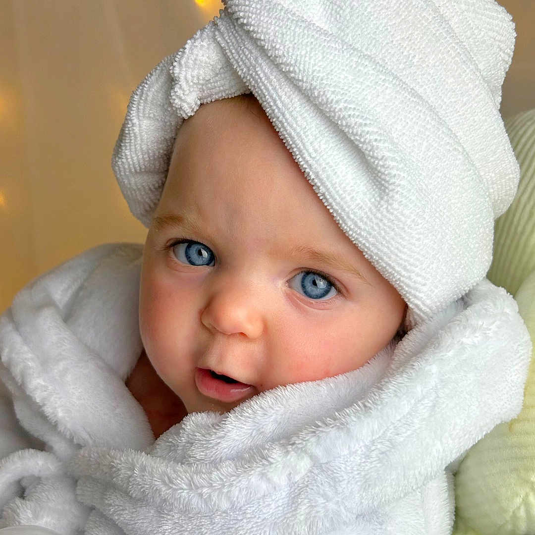 Isabella is registered to the contest to win money with this photo: baby, blue_eyes, child, closeup, cozy, curious_expression, cute, face, fairy_lights, headwear, indoor, infant, person, portrait, robe, skin, soft_lighting, towel, towel_turban, white