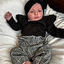 baby, infant, child, black_headband, black_top, ruffles, checkered_pants, pink_shoes, blanket, white_blanket, soft_texture, lying_down, cute, fashionable, portrait, indoors, comfort, young_child, headwear, footwear