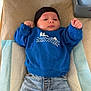 baby, child, infant, blue_sweatshirt, black_hat, jeans, rolled_up_jeans, black_socks, changing_pad, baby_care_items, expression, lying_down, indoors, skin, face, hands, clothing, person, cute, casual