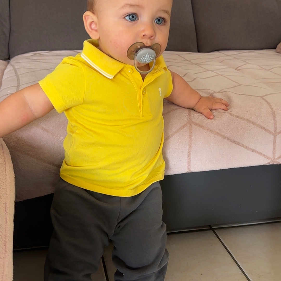 Khyronn participe au concours pour gagner de l'argent avec cette photo : baby, blue_eyes, casual_clothing, chair, child, couch, curious, furniture, home, indoor, pacifier, pants, person, portrait, socks, standing, tile_floor, toddler, yellow_polo, young_child