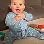 Khyronn a rejoint le concours — aidez-le/la à gagner de superbes lots ! baby, child, smiling, blue_onesie, sitting, hands_clapped, happy, indoor, couch, toy, playtime, face, cute, infant, person, expression, room, childhood, cheerful, home