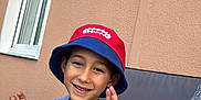 Rafael a rejoint le concours — aidez-le/la à gagner de superbes lots ! child, boy, smiling, hat, bucket_hat, tshirt, pikachu, cartoon_character, outdoor, window, wall, seated, blanket, person, hand_gesture, casual_clothing, happy, daylight, portrait, leisure