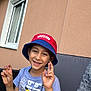 child, boy, smiling, hat, bucket_hat, tshirt, pikachu, cartoon_character, outdoor, window, wall, seated, blanket, person, hand_gesture, casual_clothing, happy, daylight, portrait, leisure