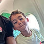 child, boy, person, smile, airplane, window, seat, green, clothing, short_hair, indoor, casual, light, adult, eyewear, portrait, seatback, travel, happy, cute