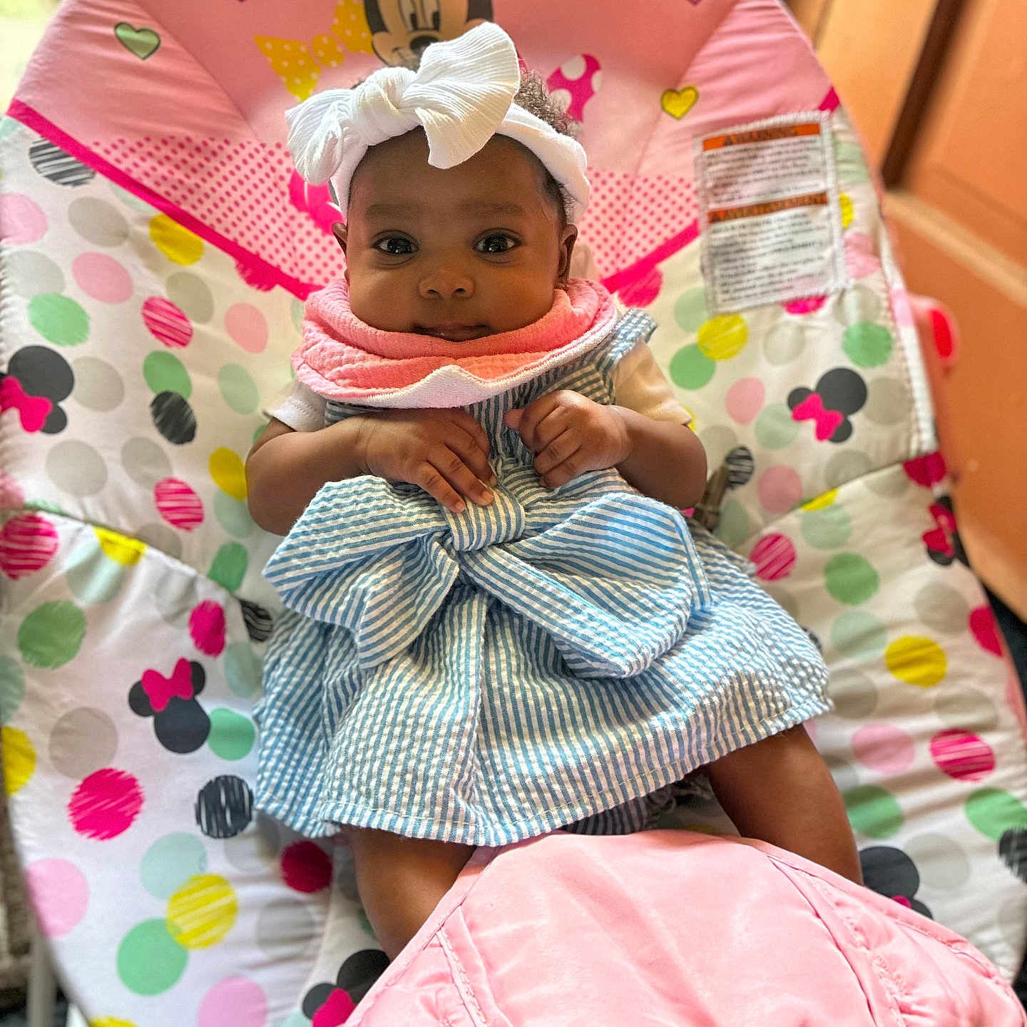 Marliyah Ava is registered to the contest to win money with this photo: baby, baby_chair, bib, bow, child, colorful, cute, dress, face, hands, headband, indoor, infant, legs, minnie_mouse, pink, polka_dots, seated, smiling, striped_dress
