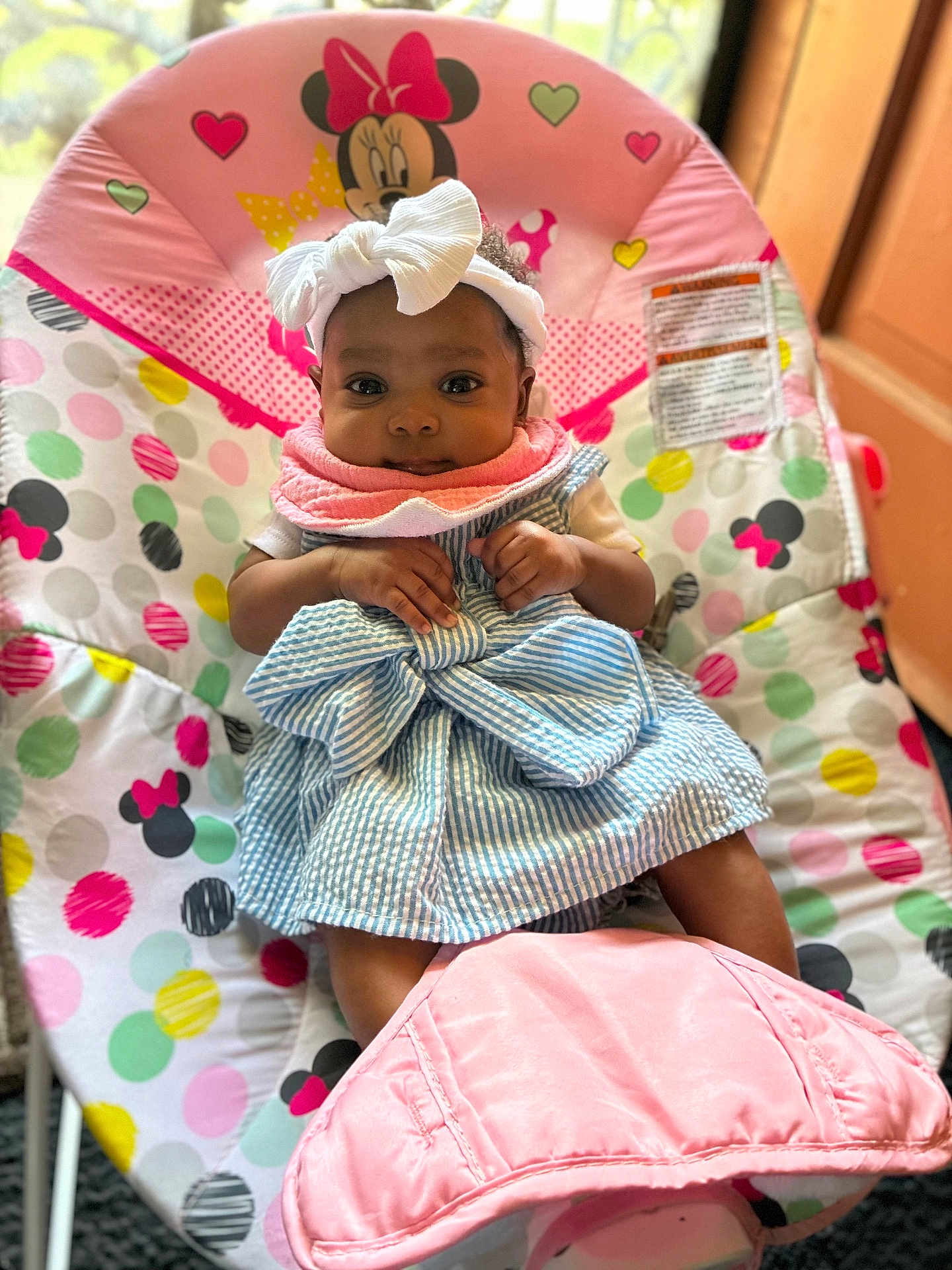 Marliyah Ava is registered to the contest to win money with this photo: baby, baby_chair, bib, bow, child, colorful, cute, dress, face, hands, headband, indoor, infant, legs, minnie_mouse, pink, polka_dots, seated, smiling, striped_dress